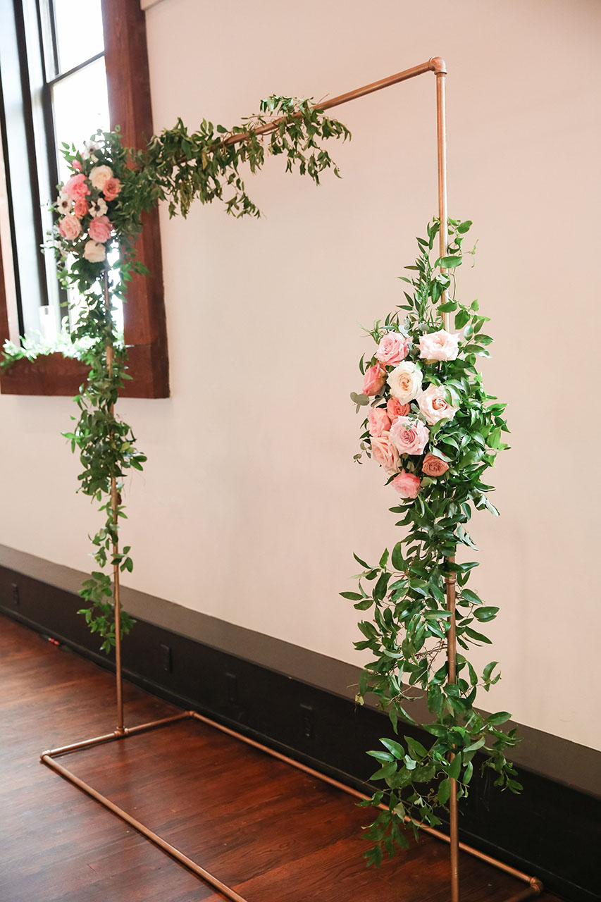 Modern metal rectangular ceremony arch wrapped in greenery and white and pink roses