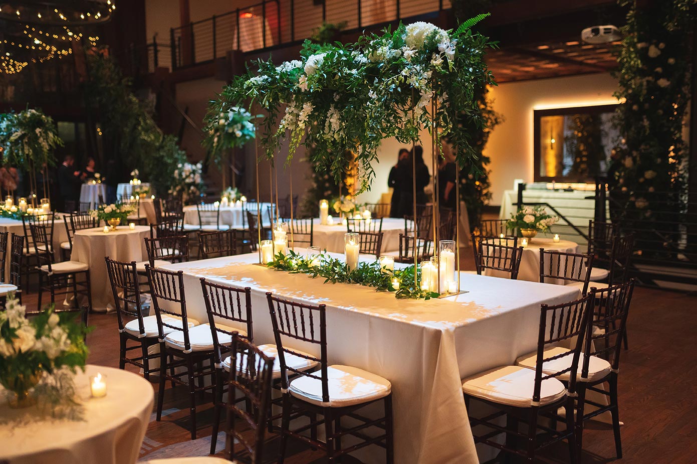Wedding reception table with modern gold stand and tall rectangular arrangement with greenery and white flowers
