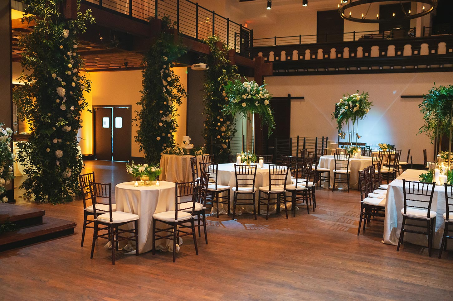 Wedding reception setup with abundant greenery wrapped around columns and tall, large arrangements as table centerpieces
