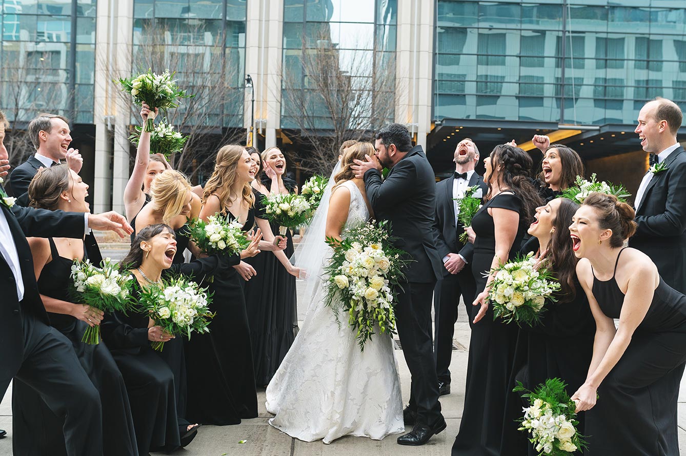 Bride and groom kiss with cheering wedding party
