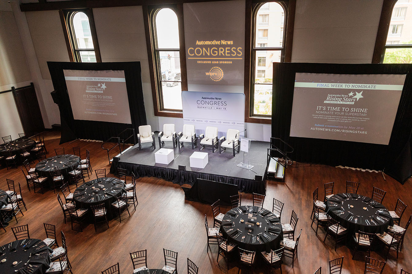 Corporate event setup with large screens, dinner tables, and talk show-style stage