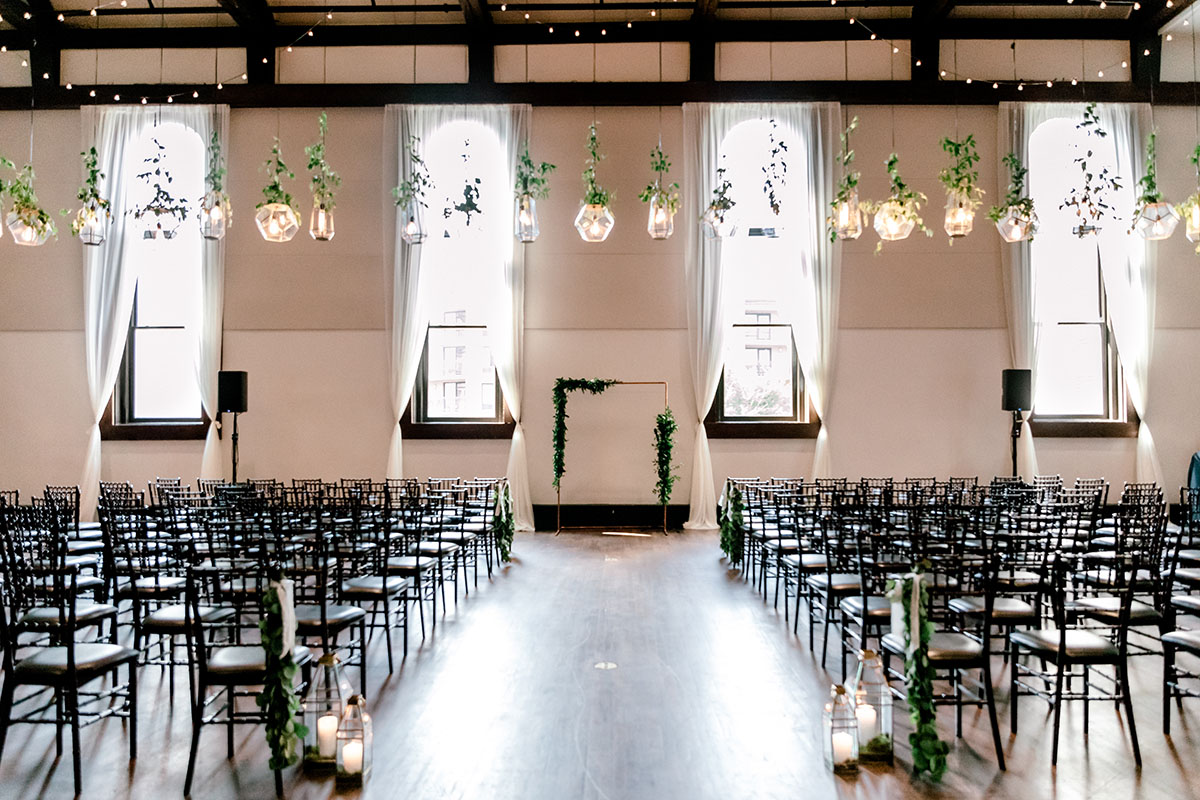 Wedding ceremony setup with greenery arch and geometric pendant lights
