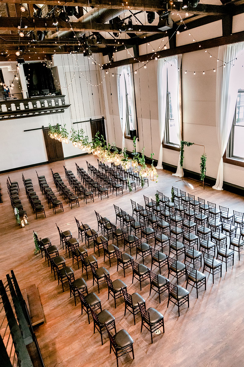 Wedding ceremony setup facing grand arched windows with geometric lights adorned in greenery